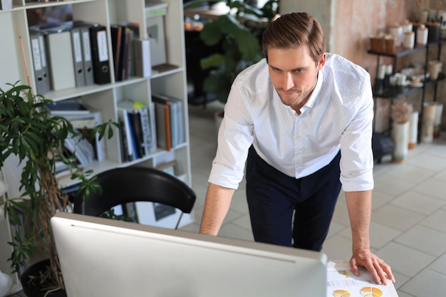 Giovane uomo d'affari moderno che analizza i dati utilizzando il computer mentre si lavora in ufficio