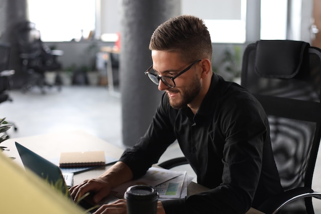 Young modern business man analyzing data using laptop while working in the office.