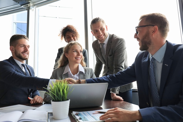 Young modern businessmen in formalwear shaking hands and smiling while working in the office.