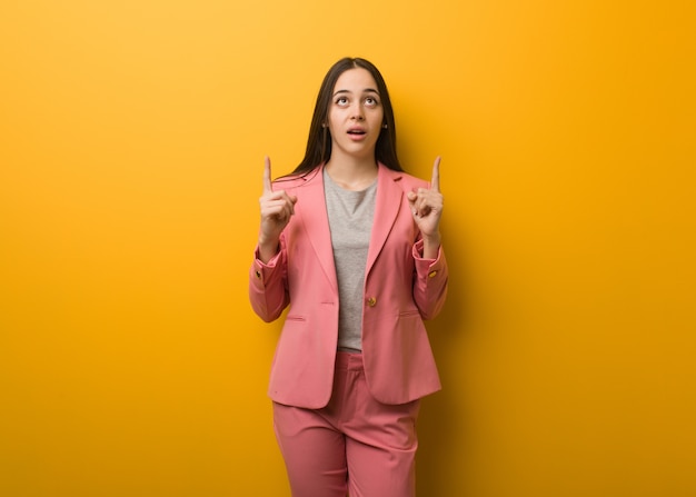 Young modern businesswoman surprised pointing up to show something