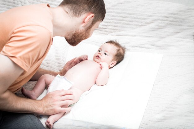 Young modern father is caring for his newborn son. Changes the diaper on the bed. Hygiene and newborn care concept. Father's love and care. Father's day.