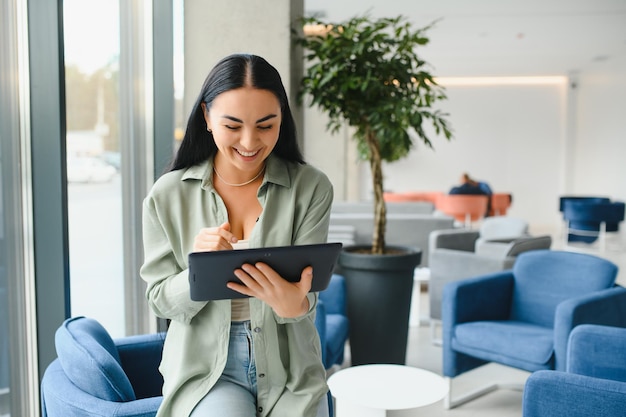 Young modern female freelancer in airport lounge or business center and works using digital tablet creating new design project