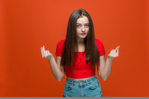 Молодая современная девушка потирает пальцы, показывая денежный жест, прося денежное вознаграждение или долг на апельсине