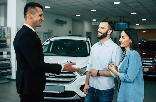 Young modern happy couple buying a new car in city dealership and talking with salesman