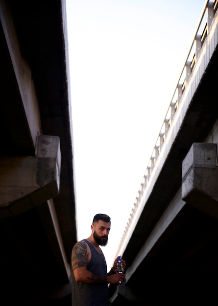 Young modern man with a beard taking a pause during his exercising outdoors in the streets to hydrate himself