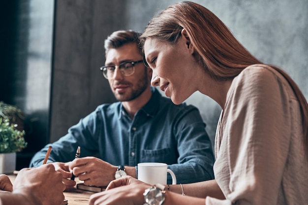 Giovani moderni in abbigliamento casual intelligente che discutono di qualcosa mentre lavorano insieme in ufficio