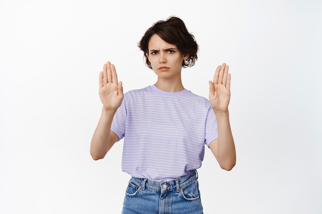 Young modern woman show block, stop no gesture, decline, rejecting something, raise palms and frowning, refusing smth bad, standing on white.