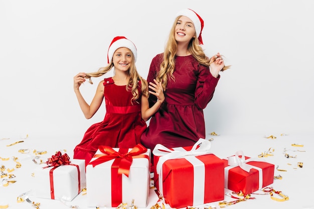 Foto giovane mamma e figlia in cappelli di babbo natale divertendosi con i regali di natale