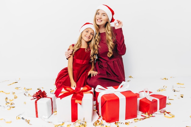 Foto giovane mamma e figlia in cappelli di babbo natale divertendosi con i regali di natale