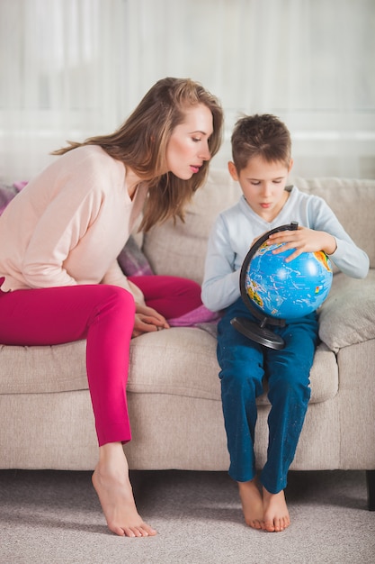 Young mom helping her son to do homework. Family choosing where to travel on vacation. Mother and her child holding a globe