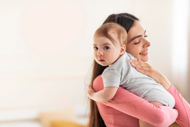 Young mom holding and hugging adorable baby enjoying motherhood\
and child care standing in bedroom at home