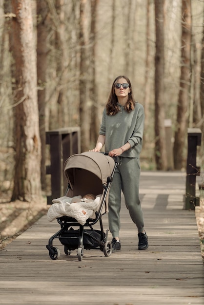 The young mom is walking on the wooden walkway with her infant child who is sleeping in the baby stroller The mother with her child in the park for fresh air