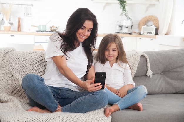 Giovane mamma e figlia piccola che giocano a giochi online a casa utilizzando uno smartphone