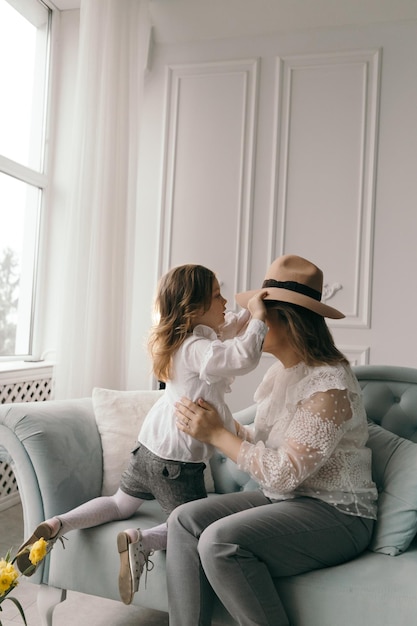 Young mom and little smiling preschooler daughter sit on couch\
in living room sharing secrets gossiping mother whisper in excited\
small girl child ear talking chatting enjoy close\
communication