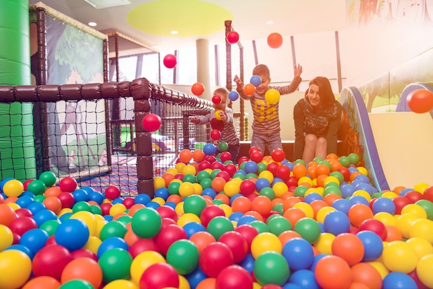 young mom playing with kids in pool with colorful balls