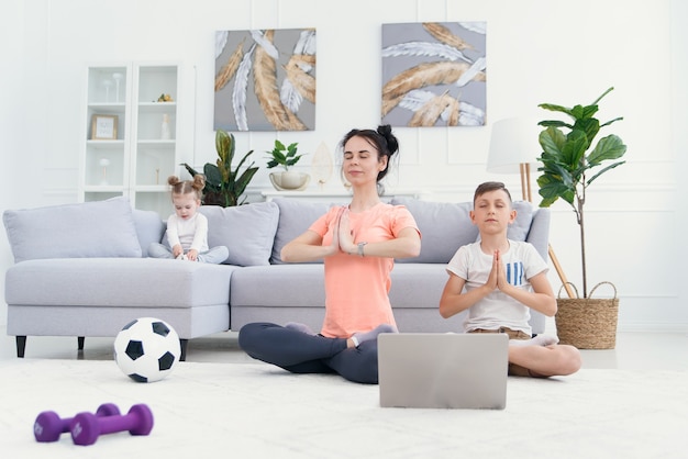 Giovane mamma e figlio praticano yoga con il computer portatile sul pavimento a casa.