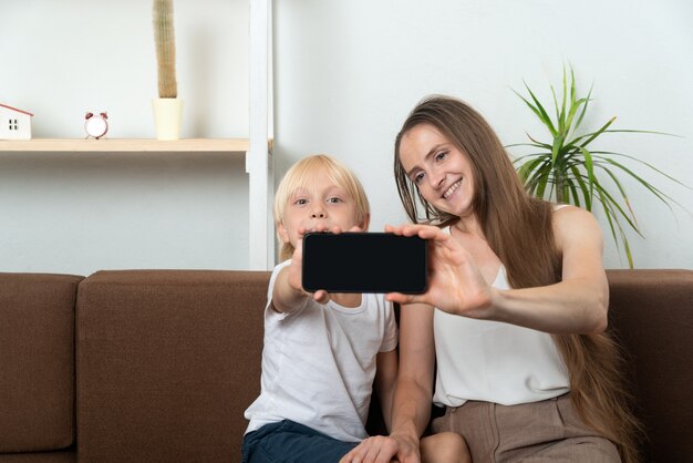 若いお母さんは息子と一緒に自分撮りをします。ママと子供がスマートフォンの画面を表示します。