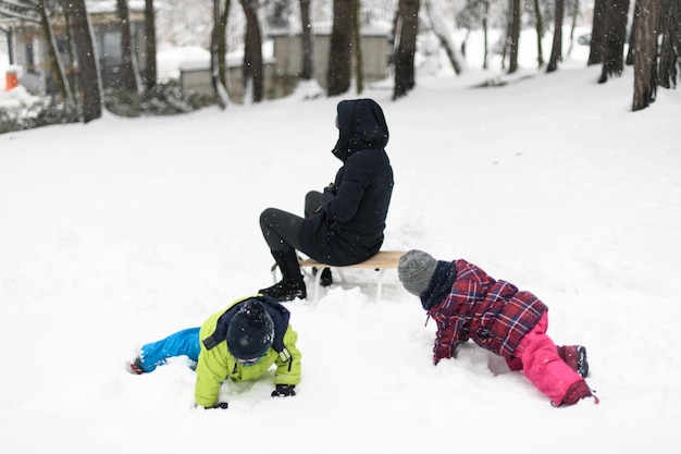 Young Mom and Two Kids Sledding in Winter Park Outdoors