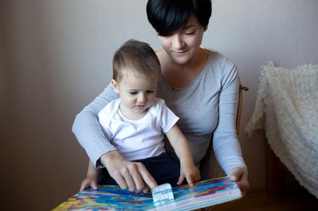 Giovane mamma con un piccolo figlio che legge un libro mentre è seduto su una sedia in camera da letto