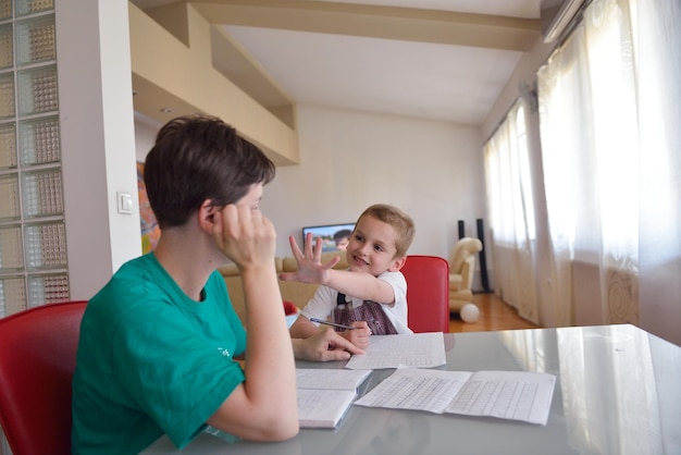 Young mom woman doing home work with elementary school grade boy at home in kitchen