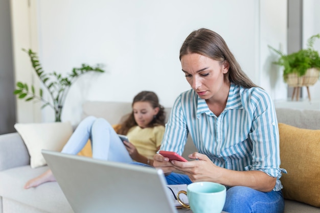 Young mom working at home with her child on the sofa while writing an email. Young woman working from home, while in quarantine isolation during the Covid-19 health crisis