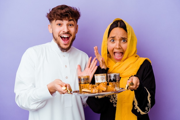 Giovane coppia marocchina bere il tè per celebrare il mese del ramadan isolato su sfondo viola