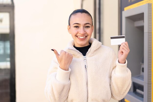 屋外でクレジット カードを保持しているモロッコの若い女の子が製品を提示する側を指しています。