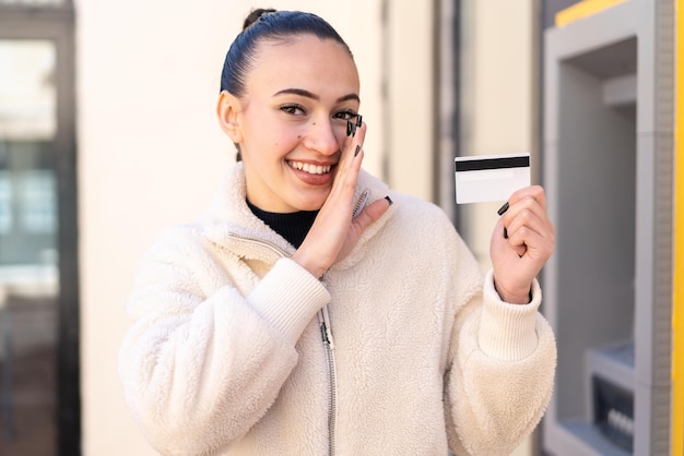 Young moroccan girl holding a credit card at outdoors whispering something