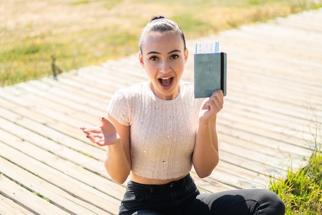 Young moroccan girl holding a passport at outdoors with shocked facial expression