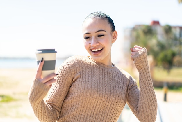 勝利を祝って屋外でテイクアウト コーヒーを保持している若いモロッコの女の子