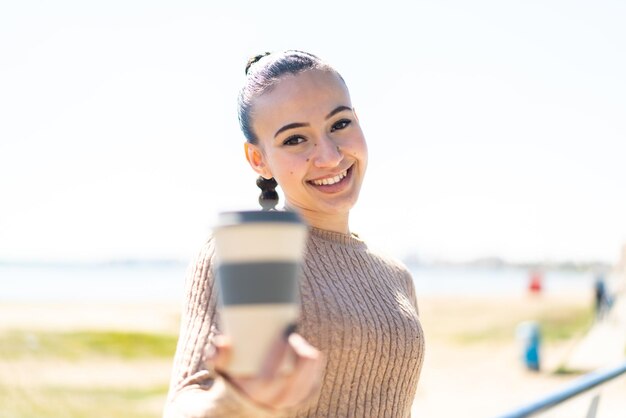 Young moroccan girl holding a take away coffee at outdoors with happy expression