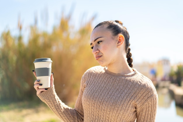 Young moroccan girl holding a take away coffee at outdoors with sad expression