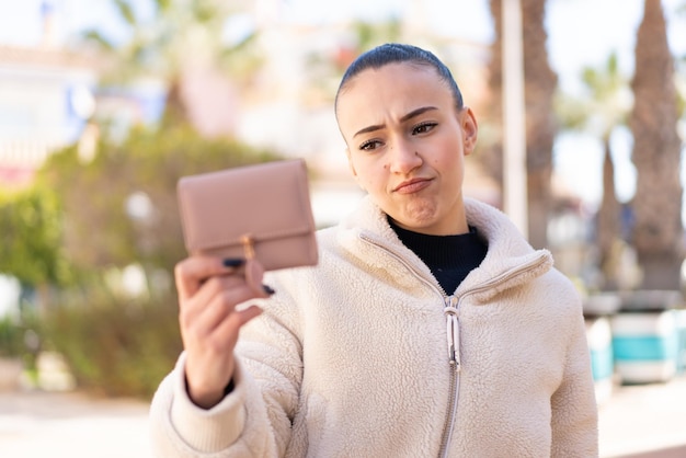 Foto giovane ragazza marocchina che tiene un portafoglio all'aperto con espressione triste