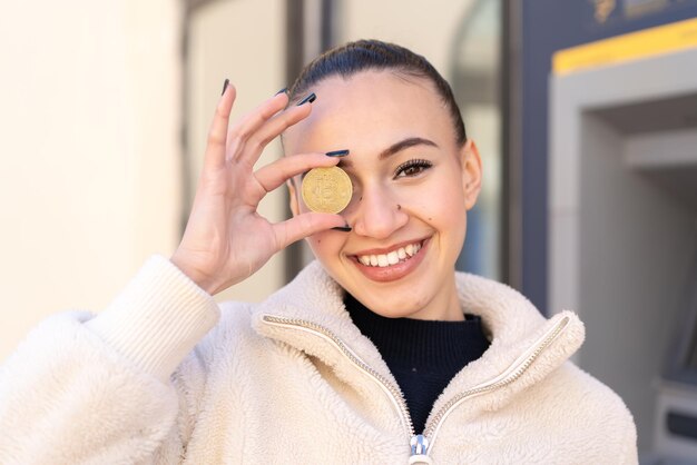 Young moroccan girl at outdoors holding a Bitcoin with happy expression