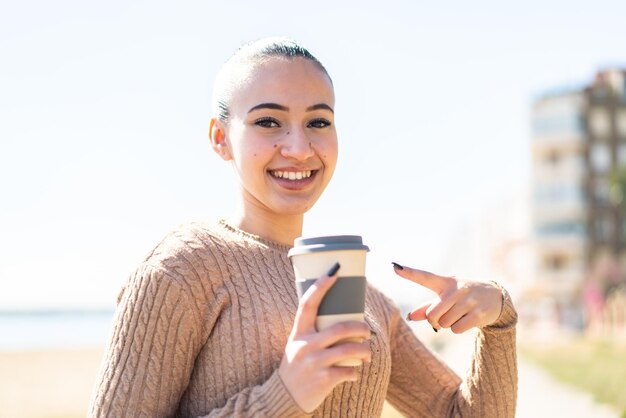 幸せな表情でテイクアウト コーヒーを保持している屋外で若いモロッコの女の子