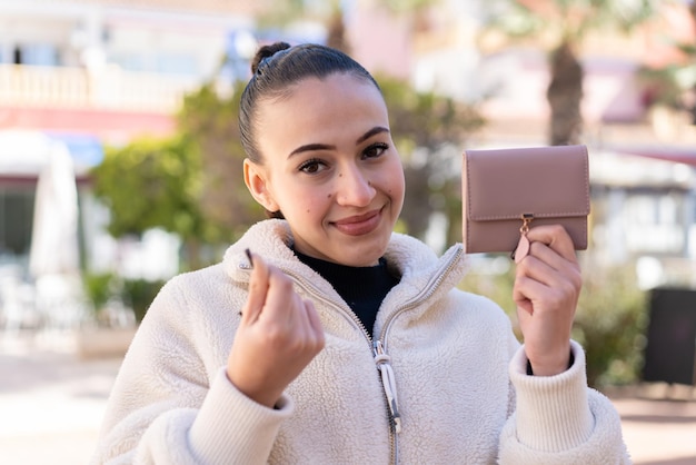 屋外でお金のジェスチャーで財布を保持している若いモロッコの女の子