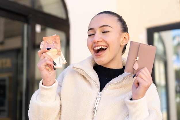 Молодая марокканская девушка на улице держит бумажник с деньгами со счастливым выражением лица