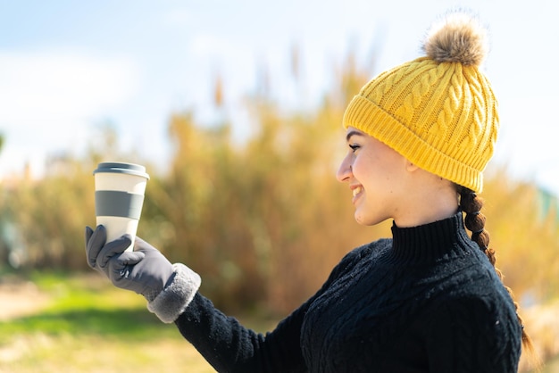 幸せな表情で屋外でコーヒーを飲みながら冬のマフを着ている若いモロッコの女の子