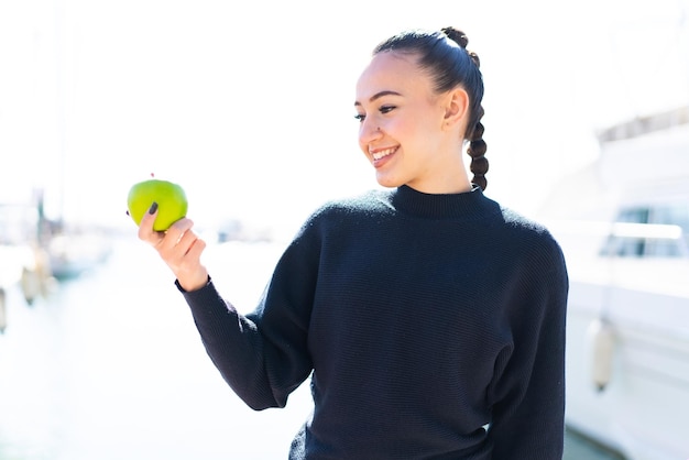 Young moroccan girl with an apple at outdoors with happy expression