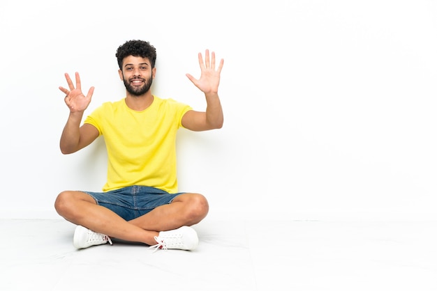 Young Moroccan handsome man sitting on the floor over isolated background counting nine with fingers