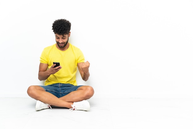 Young Moroccan handsome man sitting on the floor over isolated background surprised and sending a message