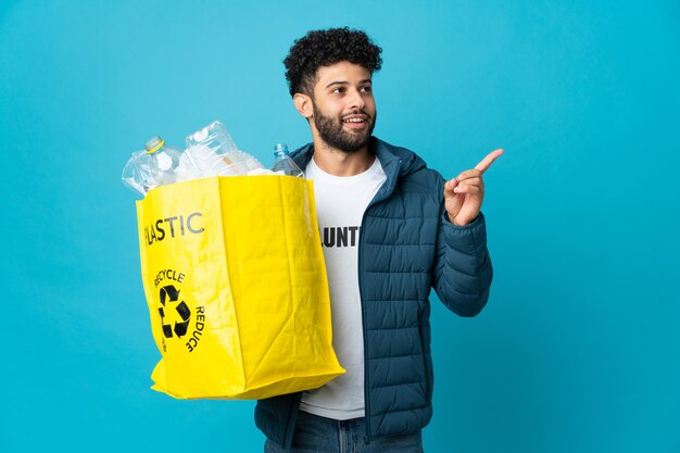 Photo young moroccan man holding a bag full of plastic bottles to recycle intending to realizes the solution while lifting a finger up