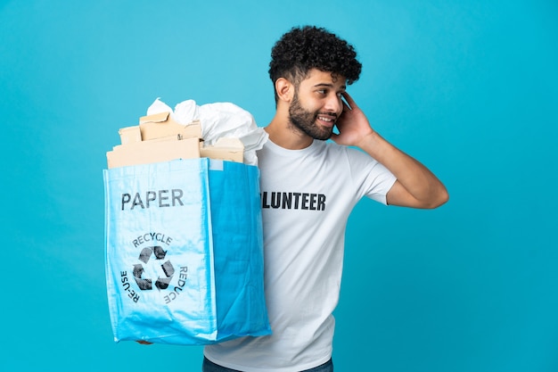 孤立したリサイクルするために紙でいっぱいのリサイクルバッグを保持している若いモロッコ人