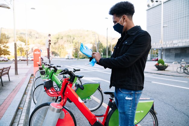 A young Moroccan man is putting on latex gloves to pick up a rented electric bicycle in the street bicycle parking lot and is wearing a face mask for the 2020 coronavirus pandemic.