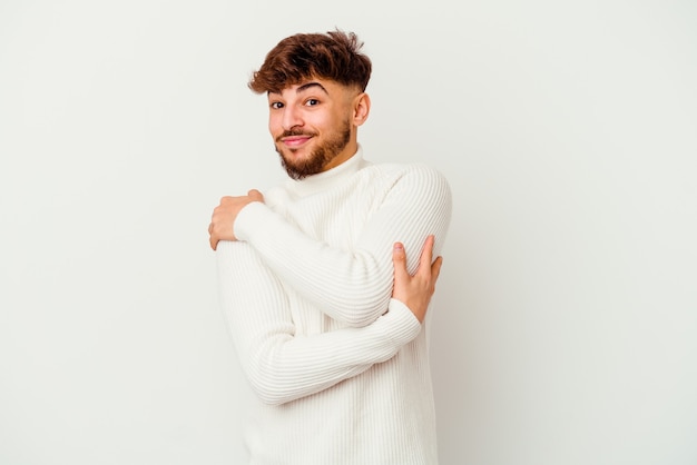 Young Moroccan man isolated on white wall hugs, smiling carefree and happy.