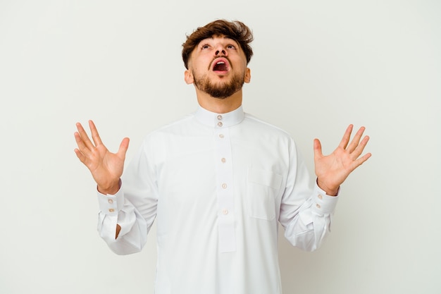 Young Moroccan man wearing a typical arab clothes isolated on white screaming to the sky, looking up, frustrated.