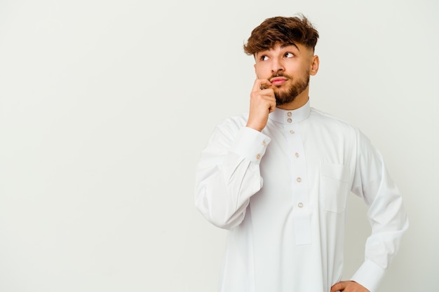 Young Moroccan man wearing a typical arab clothes isolated on white wall looking sideways with doubtful and skeptical expression.