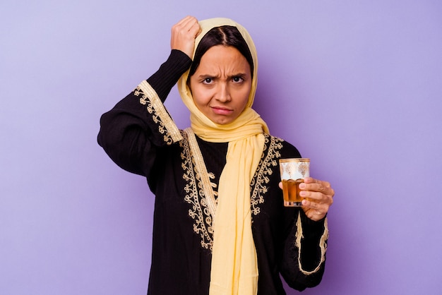 Young Moroccan woman holding a glass of tea isolated on purple background being shocked, she has remembered important meeting.