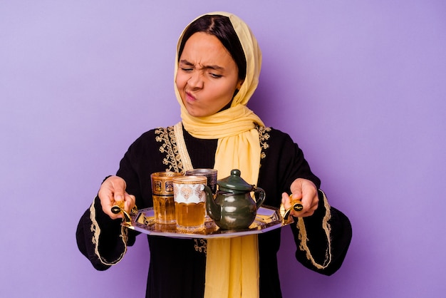 Young Moroccan woman holding a glass of tea isolated on purple background