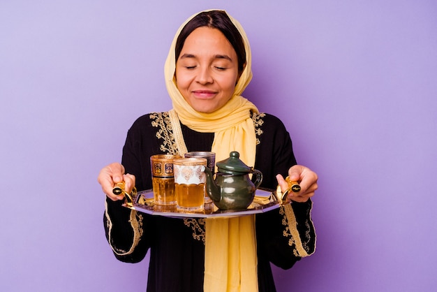 Young Moroccan woman holding a glass of tea isolated on purple background